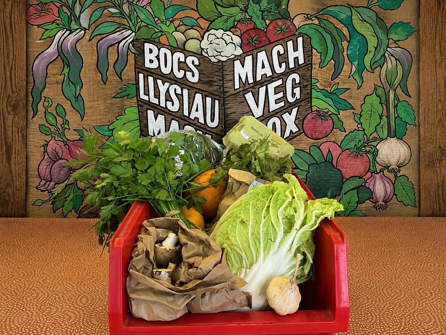 Some vegetables in a box, with Mach Veg Box poster behind